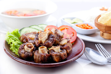 Fried oxtail with soup and white rice, chili sauce, lime, chips. Served on a plate decorated with tomatoes, cucumbers, lettuce.