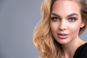 Fototapeta premium Beautiful face of an attractive model with blue eyes. Woman with beauty long brown hair and natural makeup. Closeup portrait of a caucasian female. Attractive fashion model. Beauty face of a blonde