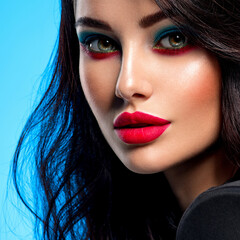 Portrait of beautiful young woman with bright blue makeup. Beautiful brunette with bright red...