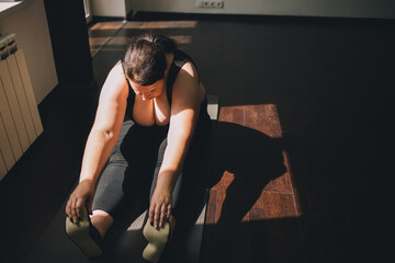 Naklejka premium Fitness, home training, flexibility. Overweight woman doing stretching exercises on a fitness mat at her living room. Healthy lifestyle
