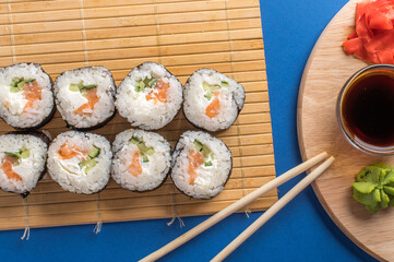 Sushi rolls set served on bamboo mat. Blue background