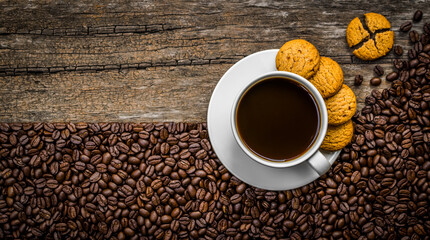 Top view of coffee in white cup with cookie on white saucer and coffee beans on wooden background.