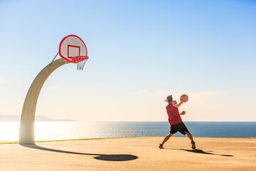 Basketball player dribbling the basket ball outdoor on a sunny day with beautiful ocean view in the background. Man playing streetball.