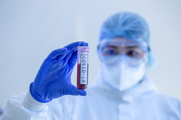 Focus on Blood test tube of COVID19, Coronavirus or Novel corona virus epidemic disease. Lab technician scientist in PPE Personal Protective Equipment holding blood tube test in hospital laboratory.