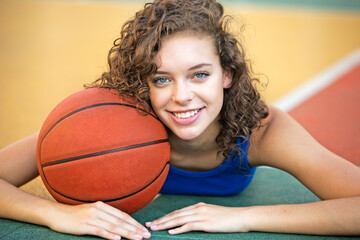 Portrait of smiling young teen girl basketball player holding a ball laying at the outdoor court....