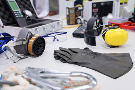 Personal Rrotection Equipment Or Safety Standard Set On Working Table. Occupational Health And Safety Tools Such As Earmuffs, Anemometer, Safety Glasses, Ruber Glove, Resperator.