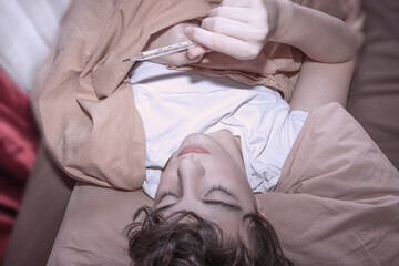 the guy lies in bed with a cold and a temperature in his hand a thermometer