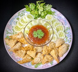 Deep-fried fish ball with dipping sauce on a white floral pattern plate.