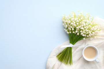 Coffee mug with bouquet of flowers lily of the valley on blue rustic table. Flat lay, top view. Beautiful breakfast, good morning concept.