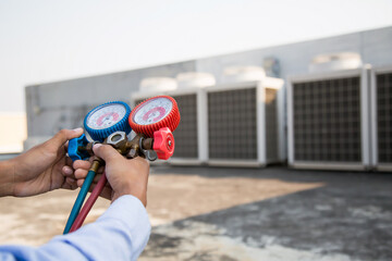 Air repair mechanic using measuring equipment for filling industrial factory air conditioners and...