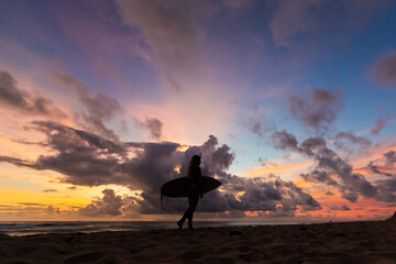 surf girl meets sunset on the beach. silhouette. a young girl with a surfboard stands on the beach and looks at a stunning sunset. multi-colored sky and clouds.