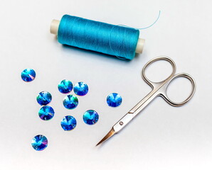 Fototapeta na wymiar Spool of blue thread, blue sequins and a pair of scissors closeup on white background