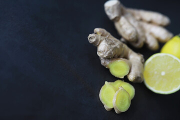 Ginger root whole and sliced. Ginger tea with lemon on the dark background. Fresh ginger root on stone background. Vitamins. Free space for your text.