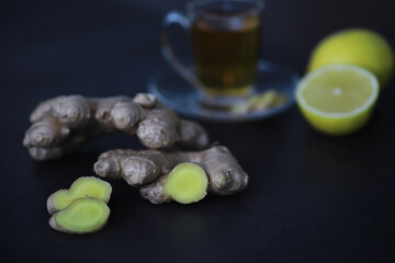 Ginger root whole and sliced. Ginger tea with lemon on the dark background. Fresh ginger root on stone background. Vitamins. Free space for your text.