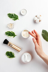 Fototapeta na wymiar Cosmetics and self-care.A woman's hand reaches for an open jar of cream. On a white background-a composition of cosmetics, accessories and leaves. Flat lay.The concept of organic and natural cosmetics