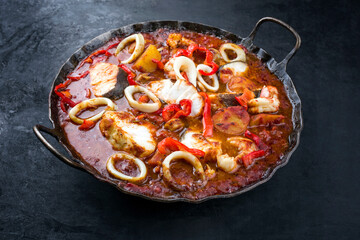 Traditioneller brasilianischer Fischeintopf Moqueca Capixaba mit Fisch Filet und Tintenfischringen in Tomaten Sauce in einer rustikalen Pfanne © HLPhoto