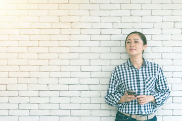 Business woman wearing a plaid shirt. In her hands holding the mobile phone and white brick wall background. Businessman with a strong and smiling face.