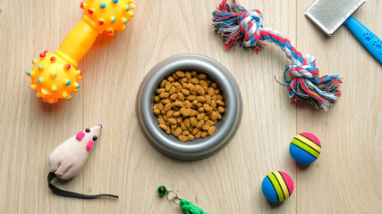 Bowl of dry food for cat or dog and pet accessories on wooden table, view from above. Pet care and training concept.