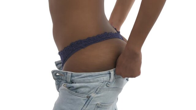 Side view of a slim young woman getting dressed. Profile view of a model wearing and zipping tight light blue skinny jeans. Isolated, on white background