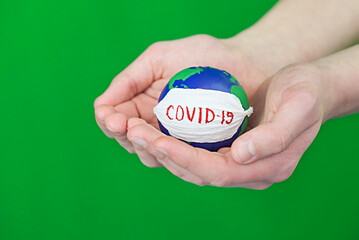 Stop corona virus. Conceptual photo of male hands holding globe with face mask on it isolated on green background
