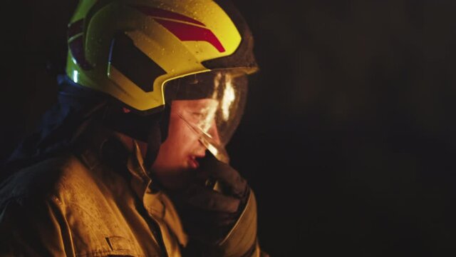 Portrait shot of a fireman in action speaking on the walkie talkie. Fire reflection on the helmet. Copy space