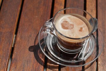 Transparent glass cup of iced coffee with ice cream in shape of heart on a wooden table in cafe outdoors top view, flat lay. Concept of rest, sweet, cold drink.
