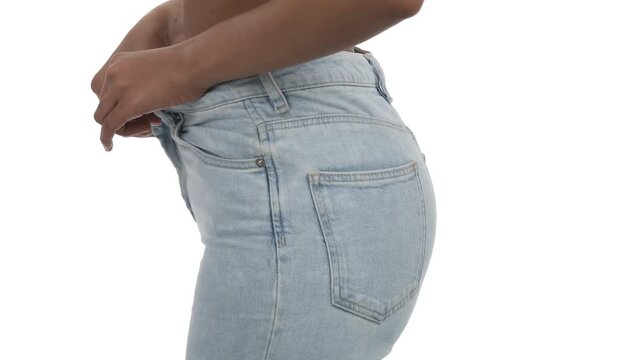 Side view of young slim African woman unbuttoning and taking off skinny jeans. Isolated, on white background