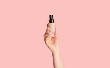 Cropped view of millennial girl showing bottle of makeup foundation on pink background