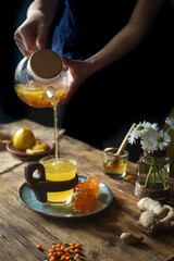 Hands are poured from a teapot into a cup of tea.
