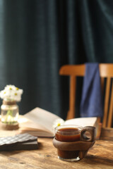 On the table is a cup of coffee, a book and a chair.
