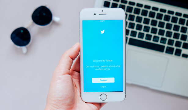 BANGKOK,THAILAND - JUNE 28, 2016: Hand holding Apple iPhone 6s showing sign up Twitter application with laptop and sunglasses in background. Twitter is largest and most popular social networking site
