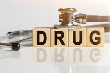 DRUG the word on wooden cubes, cubes stand on a reflective white surface, on cubes - a stethoscope.