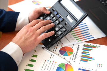 Male hand with a calculator and pen, business graph and chart.
