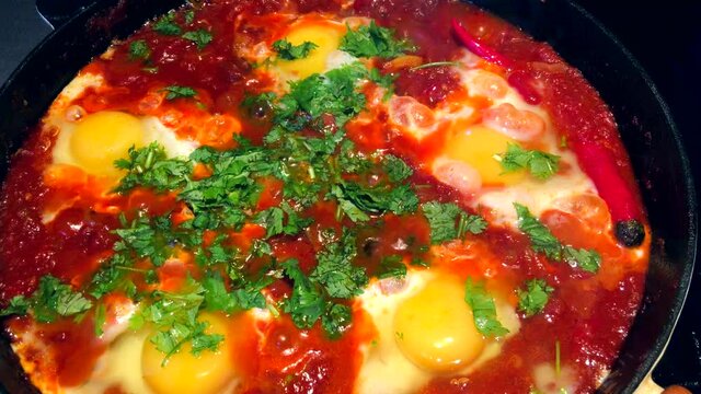 Shakshouka or shakshuka is a North African Jewish origin dish of eggs poached in a sauce of tomatoes, chili peppers, and onions, often spiced with cumin. High quality 4k footage