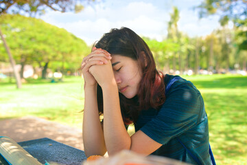 Teen girl praying outdoors at park table on sunny day - Powered by Adobe