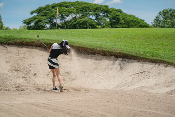 Woman golfer playing golf in sand trap on course.