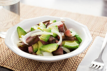 salad of black tomatoes, avocado and onions in white ceramic bowl