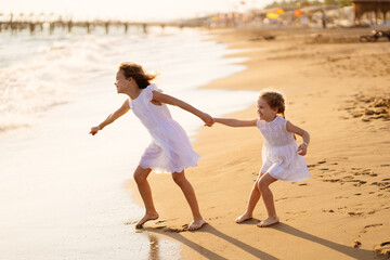 girl in white dresses playing on beach. older sister pulls younger into water.