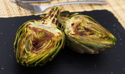 cooked fried halves artichokes on black stone board