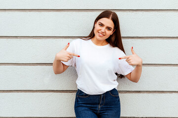 young attractive girl wearing a white t-shirt standing on a grey wall background
