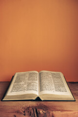 Fototapeta na wymiar Open Holy Bible on a old wooden table. Beautiful orange wall background..