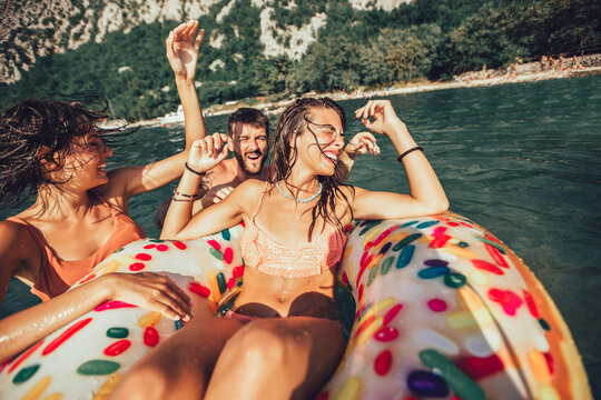 Young trendy people having fun swimming in summer vacation, relaxing on inflatable ring.