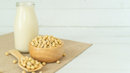 Soy milk in a bottle with soybeans in a wooden blow and scoop on white wood background with copy space. Alternative milk concept.