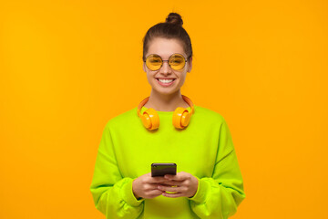 Young teenage girl in neon green sweatshirt and glasses, holding smartphone in hands, using app or...