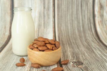Almond milk in a bottle with almonds in a wooden blow on brown wood background with copy space. Alternative milk concept.