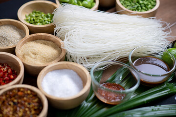 Raw rice flour in a wooden bowl with spices On a dark wood with natural light, focusing on the top of the noodles