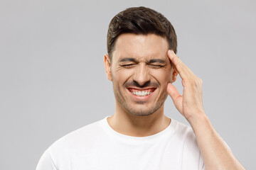 Headache concept. Man touching temple with hand trying to relieve pain, experiencing severe migraine, feeling stressed, isolated on gray background