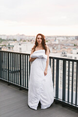 Beautiful girl on the terrace in a white blanket at sunset. Girl posing background fashion. Mood girl wrapping with blanket on balcony. Terrace mood.