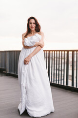Fototapeta na wymiar Beautiful girl on the terrace in a white blanket at sunset. Girl posing background fashion. Mood girl wrapping with blanket on balcony. Terrace mood.