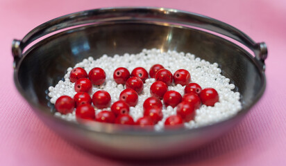 Red beads and white beads in a metal vase on a pink background